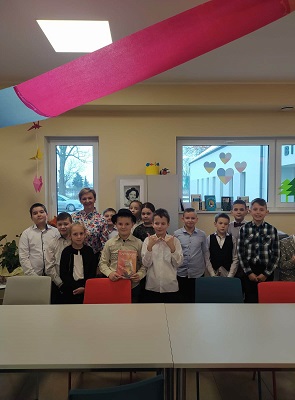Dzieci i bibliotekarka stoją za stołem ustawieni twarzami w stronę robiącego zdjęcie